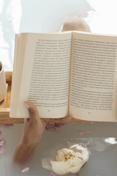 Peaceful woman relaxing in a warm bubble bath, holding a cup of tea and reading a book
